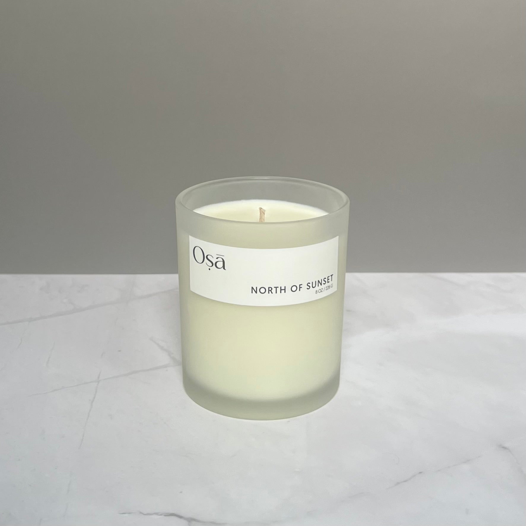 A candle on a countertop with a label displaying Osa North of Sunset.