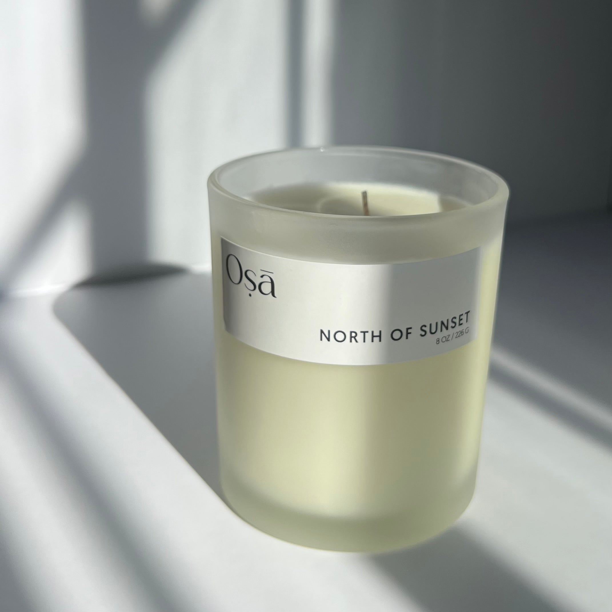 A candle in the sunlight with a label that displays Osa North of Sunset.