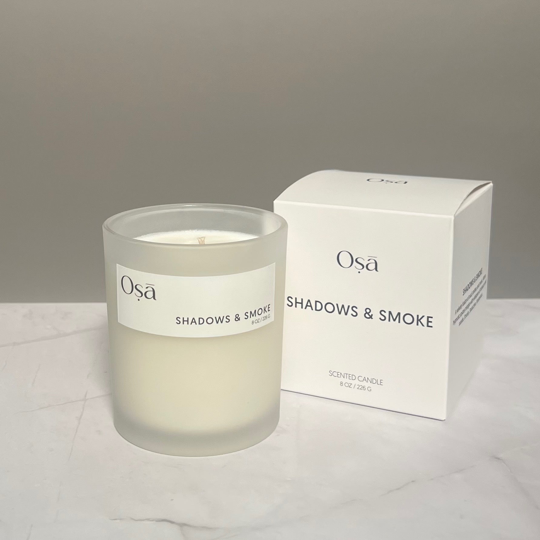 A candle next to a box with a label displaying Osa Shadows & Smoke.